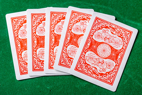 Konzeptbild zum Thema Glücksspiel zeigt fünf verdeckte Spielkarten, vor dem Start des Spiels, auf einer grünen Oberfläche